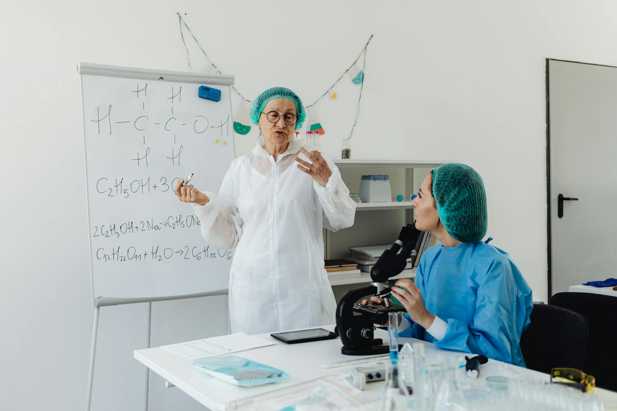 Female scientists in protective gear discussing chemical formulas in a laboratory.